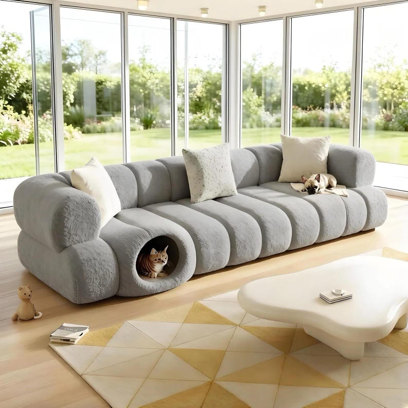 May include: A large, gray, modern sofa with a built-in cat bed. The sofa has a rounded design and is adorned with several throw pillows. A cat is inside the cat bed. A small dog rests on the sofa. The sofa sits on a patterned rug.
