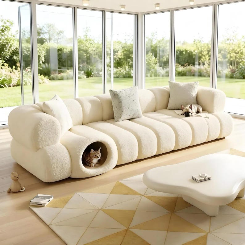 May include: A cream-colored, modern sectional sofa with a built-in cat bed. The sofa has a rounded, ribbed design and includes several throw pillows. A small dog and a cat are on the sofa. A white coffee table and a geometric rug are in front of the sofa.