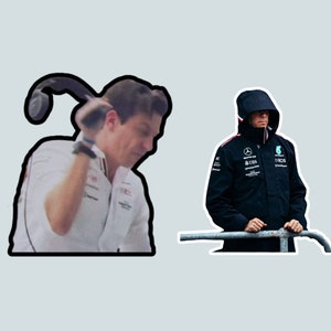 May include: Two men, one wearing a white shirt and the other wearing a black jacket with the Mercedes-AMG Petronas Formula One Team logo, stand in front of a gray background.