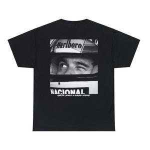 Op de afbeelding: Zwart t-shirt met een zwart-wit afbeelding van het gezicht van een autocoureur, met het woord "Marlboro" op de helm. Het woord "NACIONAL" staat onder de afbeelding, samen met "AYRTON SENNA A RACING LEGEND."