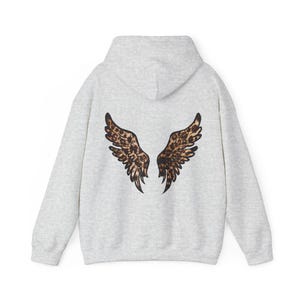 May include: A light gray hoodie with a hood and long sleeves. The back of the hoodie features a pair of stylized wings with a brown and black leopard print pattern. The wings are symmetrical and spread out.