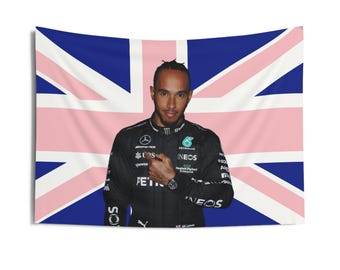 Peut inclure: Une combinaison de course noire et verte avec le texte "INEOS" et "PETRONAS" sur le devant. La combinaison est portée par une personne debout devant un drapeau britannique.