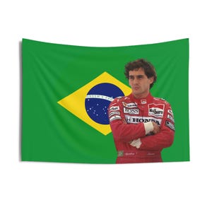 May include: A red racing suit with the words "Malboro", "Boss", and "Honda" on it. The suit is worn by a man standing in front of a green and yellow Brazilian flag with the words "Ordem e Progresso" on it.