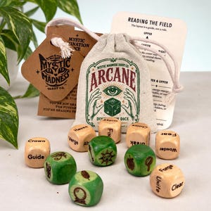 Pode incluir: Um conjunto de dados de adivinhação de madeira num saco bege com cordão, com o texto ARCANE e um gráfico de um olho. Os dados são de madeira clara e verde, com vários símbolos e palavras como Crown, Guide, Storm, Forge e Unite. Inclui uma etiqueta castanha e um cartão de instruções branco.