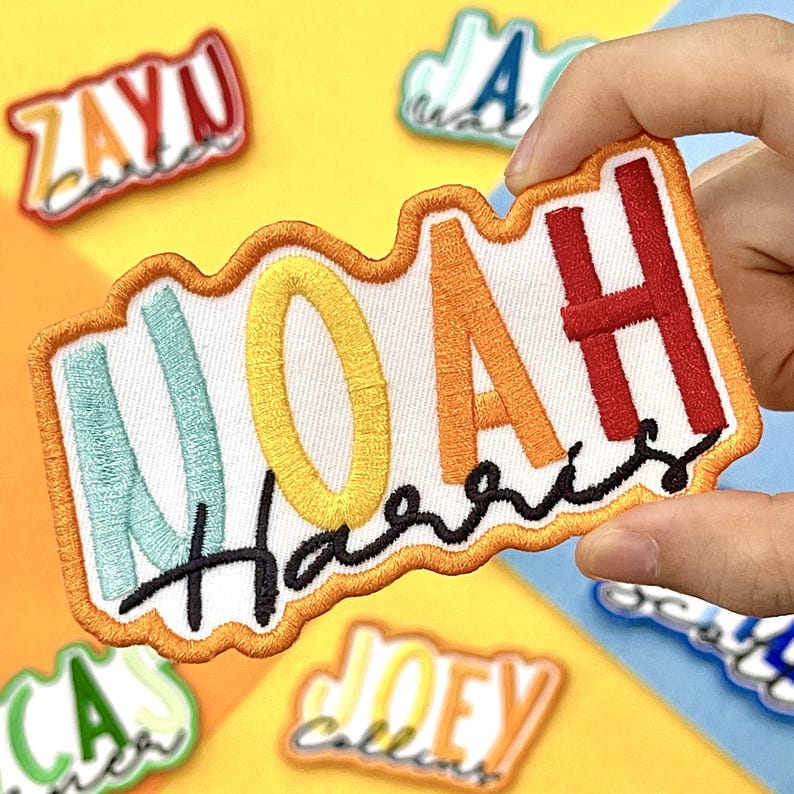 Puede incluir: Parche bordado con el nombre "Noah Harris" en letras coloridas. El parche tiene un fondo blanco con un borde naranja. Otros parches con nombres son visibles en el fondo.