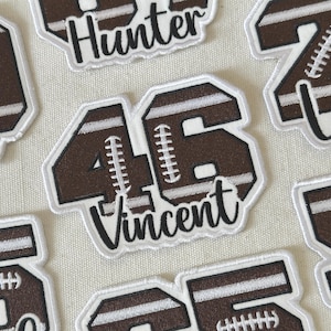 May include: Brown and white football-themed patches with the number 46 and the name "Vincent". Other patches include the name "Hunter" and numbers. The patches have a white border and are on a light-coloured fabric.