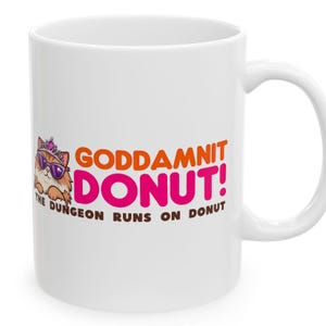 May include: White ceramic mug with a handle featuring the text "GODDAMNIT DONUT!" in orange and pink. A cartoon cat wearing sunglasses and a crown is on the left. The phrase "THE DUNGEON RUNS ON DONUT" is below the main text.
