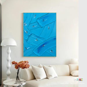 Op de afbeelding: Een rechthoekig wandkunstwerk met dikke, getextureerde blauwe verfstreken op het doek. Kleine, donkere silhouetten van figuren op surfplanken zijn verspreid over de compositie, wat een gevoel van beweging cre&euml;ert op het blauwe oppervlak.