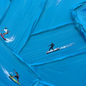 Op de afbeelding: Een olieverfschilderij met dikke, getextureerde blauwe impasto-penseelstreken die oceaangolven voorstellen. Vier kleine figuren surfen op kleurrijke planken over het oppervlak, wat witte waterspatten en bewegingssporen in de verf cre&euml;ert.