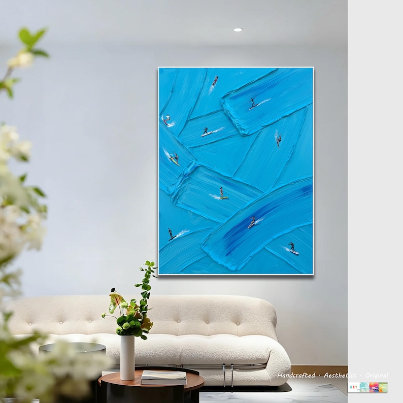 Op de afbeelding: Een rechthoekig wandkunstwerk met een levendige blauwe achtergrond en dikke, getextureerde verfstreken. Kleine, donkere figuren van mensen op surfplanken zijn verspreid over het doek en lijken over de verhoogde randen van de blauwe verf te rijden.