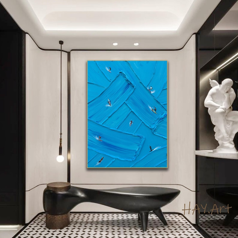 Puede incluir: Un cuadro rectangular sobre lienzo con pinceladas gruesas y texturizadas en varios tonos de azul brillante. Peque&ntilde;as figuras abstractas de surfistas sobre tablas est&aacute;n dispersas por la superficie, creando una sensaci&oacute;n de movimiento.