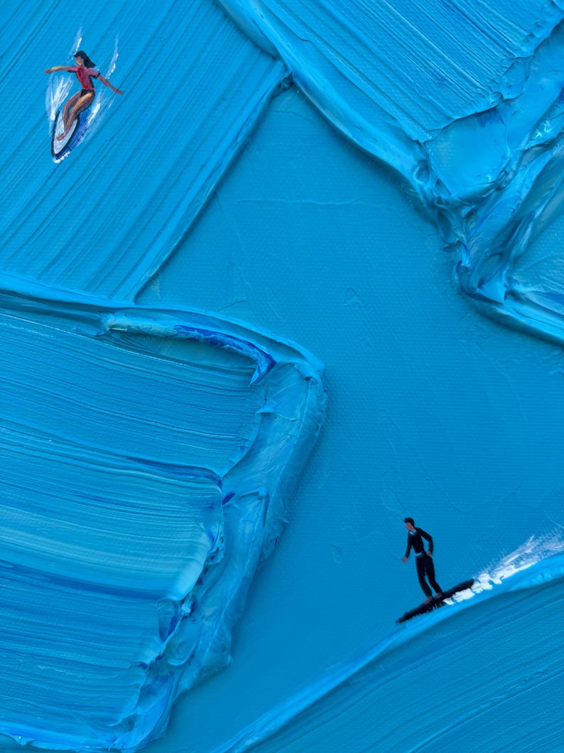 Puede incluir: Una pintura al &oacute;leo sobre lienzo con pinceladas de impasto azul gruesas y texturizadas que crean un efecto de ola. Se representan dos figuras peque&ntilde;as: una persona con una parte superior roja surfeando y otra con un traje negro sobre una tabla.