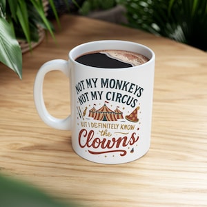 May include: White ceramic mug with a black coffee fill. The mug features the text "NOT MY MONKEYS NOT MY CIRCUS BUT I DEFINITELY KNOW the CLOWNS" in a mix of fonts and colors, with circus-themed graphics.