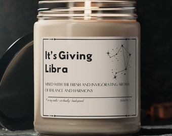 Könnte beinhalten: Eine beige Kerze mit einem schwarz-weißen Etikett, auf dem "It's Giving Libra" steht und ein Librasymbol abgebildet ist. Die Kerze befindet sich in einem durchsichtigen Glasgefäß mit einem schwarzen Deckel.