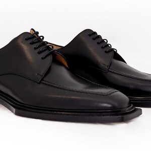 May include: A pair of black leather dress shoes with a square toe design. The shoes have a classic lace-up closure and a low heel. The leather appears smooth and polished, suitable for formal occasions.