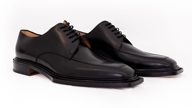 May include: A pair of black leather dress shoes with a square toe design. The shoes have a classic lace-up closure and a low heel. The leather appears smooth and polished, suitable for formal occasions.
