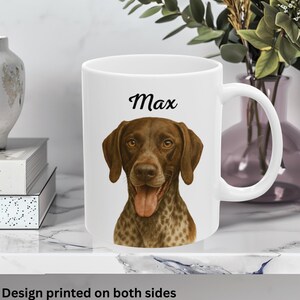May include: A white ceramic mug with a black handle and the text "But First, Coffee" in a bold, black font. The mug is set against a blurred background. The mug appears to be approximately 10 cm tall.