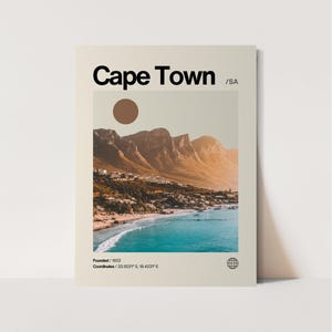 May include: A vintage-style poster featuring a scenic view of Cape Town, South Africa. The poster has a brown background with the text "Cape Town /SA" in black at the top. The image shows a mountain range with a beach and ocean in the foreground. The text "Founded/1652" and "Coordinates/33.9221" S, 18.4231°E" is at the bottom of the poster.