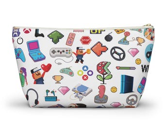 May include: A white zippered pouch with a colorful pattern of video game icons, including controllers, characters, and game consoles. The pattern includes the words "STOP", "UP", and "Wii".