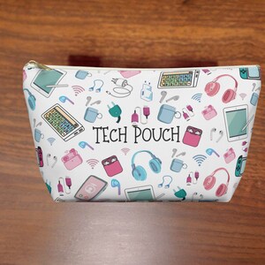 May include: White zippered pouch with a colorful print of various tech items, including headphones, chargers, and phone cases. The text "TECH POUCH" is printed in black on the front.