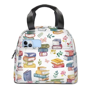 May include: White lunch bag with a black handle and zipper. The bag is covered in a watercolor pattern of stacked books in various colors, butterflies, and floral accents. A light blue phone is in the front pocket.