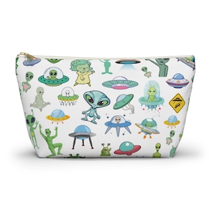 May include: A white zippered pouch with a repeating pattern of green aliens and flying saucers. The aliens are in various poses, including waving, sitting, and standing. The flying saucers are in various shapes and sizes.