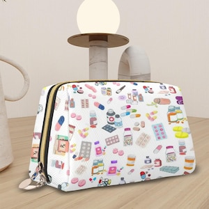 May include: White cosmetic bag with a gold zipper, adorned with a colorful pattern of various pills, capsules, and medicine bottles. The bag is rectangular and sits on a wooden surface.