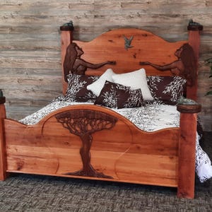 May include: A wooden bed frame with a carved tree design and two figures on the headboard. The bed is made of natural wood and has a rustic look. The bed is covered in a white and black patterned bedding.
