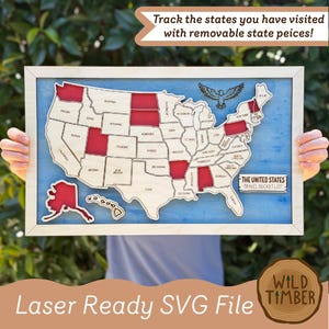 May include: A wooden map of the United States with a blue background and a light wood frame. The map features removable state pieces, with some states highlighted in red. It includes an eagle graphic and a sign reading THE UNITED STATES TRAVEL BUCKET LIST.