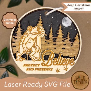 May include: Wooden Christmas ornament with a frog holding a flower, set against a forest and night sky. The ornament has the words "Believe", "Protect and Preserve", and "Keep Christmas Weird!" Laser Ready SVG File.