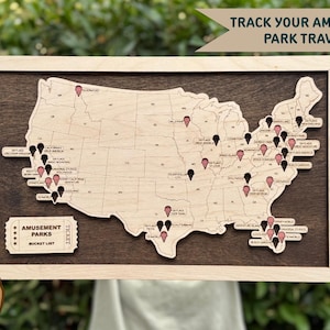 Könnte beinhalten: Holzkarte der Vereinigten Staaten mit durch Pins markierten Freizeitpark-Standorten. Die Karte ist in hellem Holz gerahmt und vor einem dunklen Holzgrund platziert. Der Text lautet "Verfolge deine Freizeitpark-Reisen!" und "Freizeitpark-Bucket-Liste".