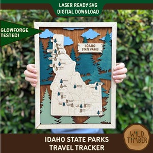 Peut inclure: Tableau de voyage en bois des parcs d'État de l'Idaho, avec un cadre en bois clair. La carte présente un design découpé au laser avec des accents bleus, verts et bruns. Le texte "IDAHO STATE PARKS TRAVEL TRACKER" est affiché en bas.