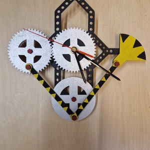 Op de afbeelding: Een klok met een zwart en zilveren tandwielontwerp. De wijzerplaat van de klok is wit met zwarte wijzers en een rode secondewijzer. De klok is gemonteerd op een houten oppervlak.