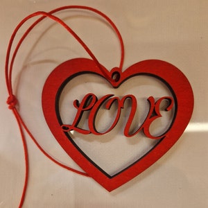 May include: Red wooden heart-shaped ornament with a cutout of the word "LOVE" inside. The ornament has a red string attached for hanging.