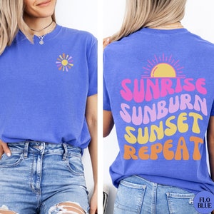 May include: A blue t-shirt with a graphic of a sun and the text "Sunrise Sunburn Sunset Repeat" in pink, orange, and yellow.