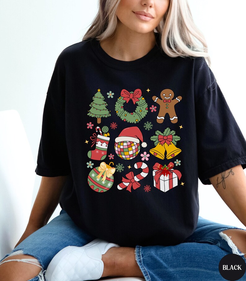 May include: A black short-sleeved t-shirt featuring a colourful graphic print of various Christmas icons including a tree, wreath, gingerbread person, stocking, disco ball with a Santa hat, bells, ornament, candy cane, and a gift box.