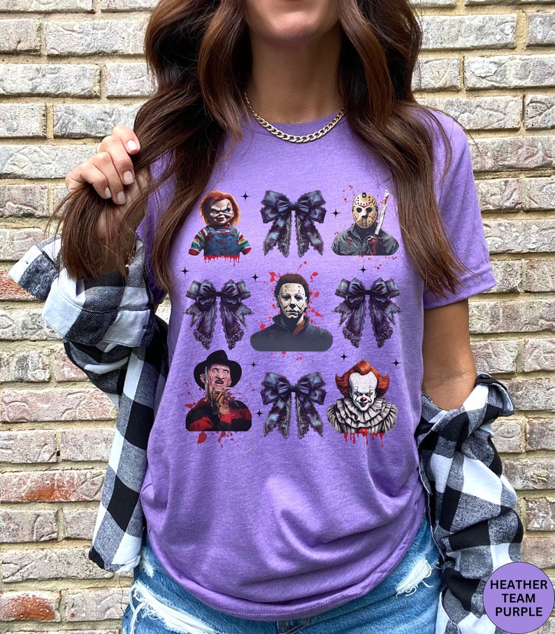 May include: Purple t-shirt featuring a collage of horror movie characters and black bows. The design includes images of Chucky, Jason Voorhees, Michael Myers, Freddy Krueger, and Pennywise, with blood splatter accents.