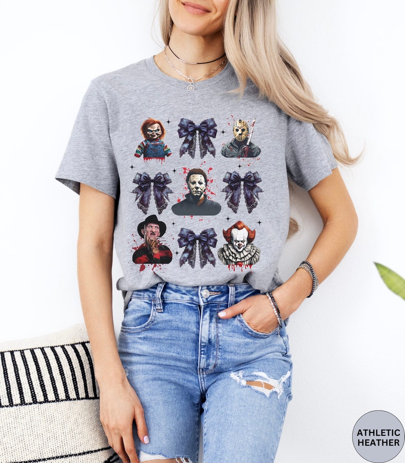 May include: Athletic heather gray t-shirt featuring a grid of horror movie characters and black bows. The characters include Chucky, Jason Voorhees, Michael Myers, Freddy Krueger, and Pennywise. The shirt is made of a soft, comfortable material.