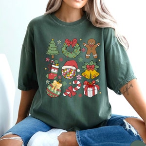 May include: A dark green short-sleeve t-shirt featuring a grid of colourful Christmas-themed illustrations including a tree, wreath, gingerbread person, stocking, disco ball with a Santa hat, bells, ornament, candy cane, and a gift box.