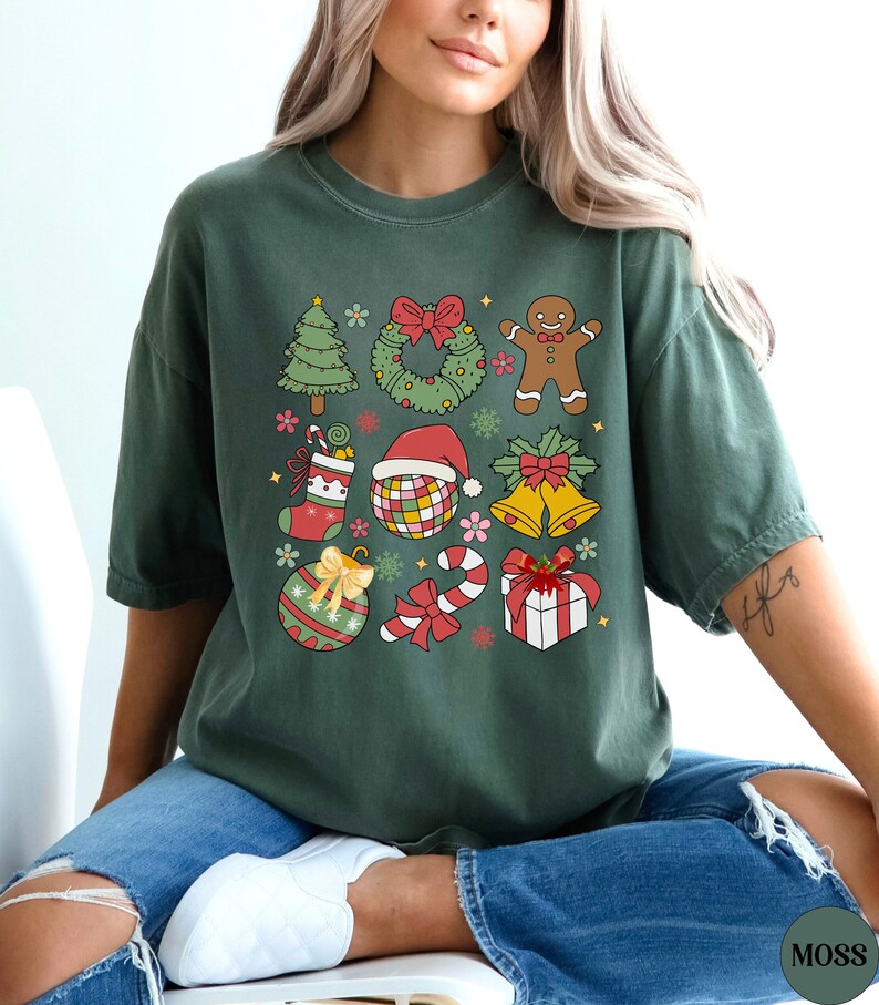 May include: A dark green short-sleeve t-shirt featuring a grid of colourful Christmas-themed illustrations including a tree, wreath, gingerbread person, stocking, disco ball with a Santa hat, bells, ornament, candy cane, and a gift box.