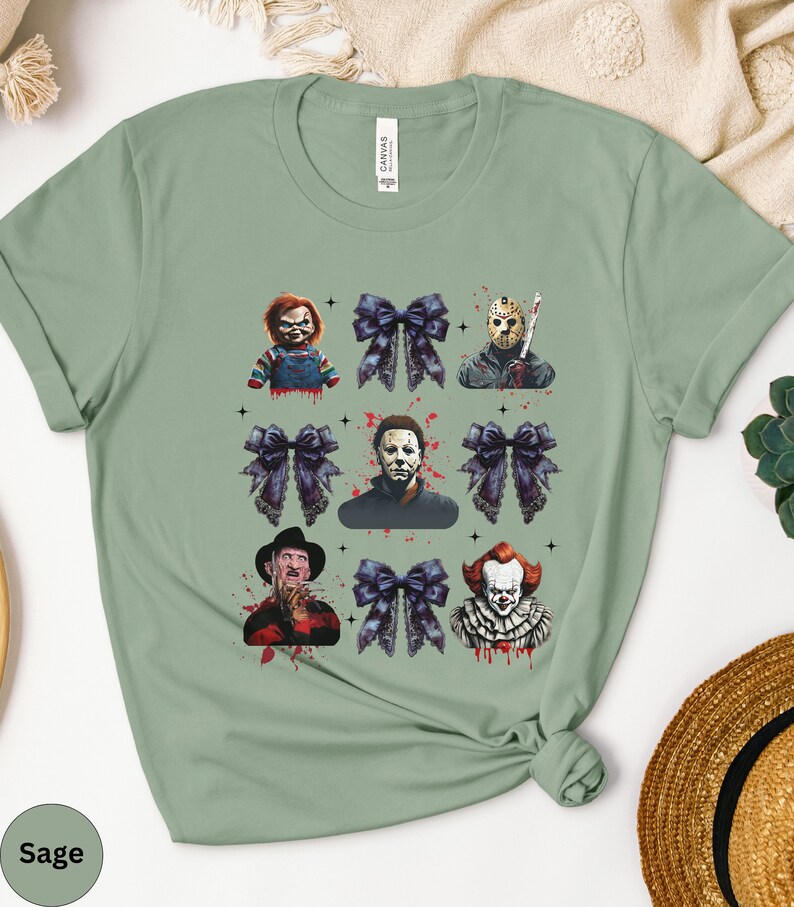 May include: Sage green t-shirt featuring a grid design with horror movie characters and dark blue bows. The characters include Chucky, Jason Voorhees, Michael Myers, Freddy Krueger, and Pennywise. The word "Sage" is printed on the bottom left.