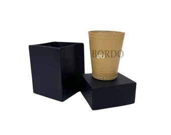 Könnte beinhalten: Ein beiger Leder-Schnapsglas mit dem Aufdruck "BORDO" in einer schwarzen Box.