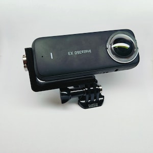 May include: A black Insta360 EX camera with a GoPro mount. The camera has a lens on the right side and the text "Insta360 EX" on the left side.