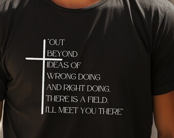 May include: Black t-shirt with white text and a cross graphic. The text reads "OUT BEYOND IDEAS OF WRONG DOING AND RIGHT DOING. THERE IS A FIELD. I'LL MEET YOU THERE."