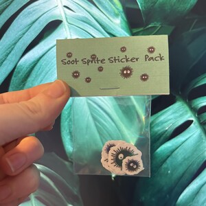 May include: A small clear plastic bag containing several black and white soot sprite stickers. A white card attached to the bag reads "Soot Sprite Sticker Pack".