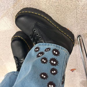 May include: Black leather boots with yellow stitching and a pair of blue jeans with black and white embroidered characters.