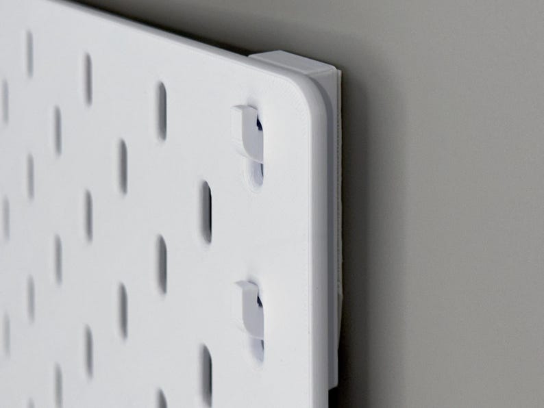 Peut inclure: Un panneau perfor&eacute; rectangulaire blanc dot&eacute; d'une grille de fentes ovales verticales r&eacute;guli&egrave;rement espac&eacute;es. Le panneau est fix&eacute; avec un bloc d'espacement blanc &eacute;pais dans le coin, cr&eacute;ant un petit espace entre la plaque et le mur.