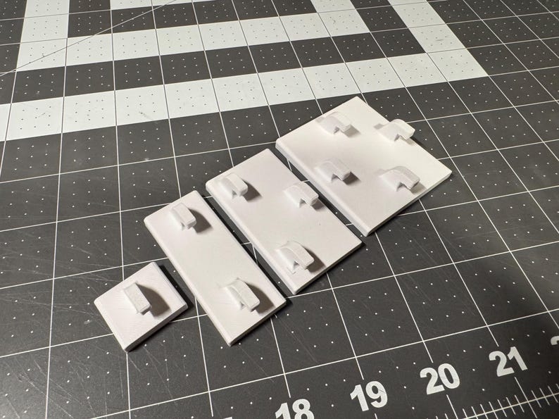 May include: A collection of white jewelry display cards in various sizes, each featuring a raised, curved holder. The cards are arranged on a black and white grid surface, providing a clean and organized presentation for showcasing earrings or other small jewelry items.