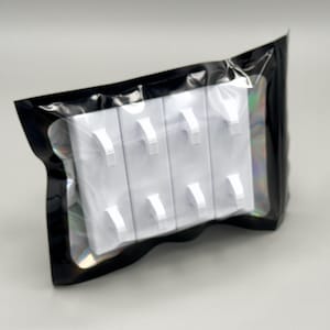 Peut inclure: Un ensemble de quatre crochets muraux rectangulaires en plastique blanc, chacun dot&eacute; de deux tiges incurv&eacute;es, scell&eacute; dans une pochette en plastique noir avec une fen&ecirc;tre transparente qui r&eacute;v&egrave;le le contenu &agrave; travers la face avant de l'emballage.