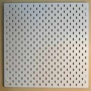 Peut inclure: Un panneau perfor&eacute; carr&eacute; de couleur blanche pr&eacute;sentant une grille uniforme de fentes verticales en forme de rectangle arrondi. Le panneau comporte quatre petits trous de fixation situ&eacute;s pr&egrave;s de chaque coin pour le montage mural.